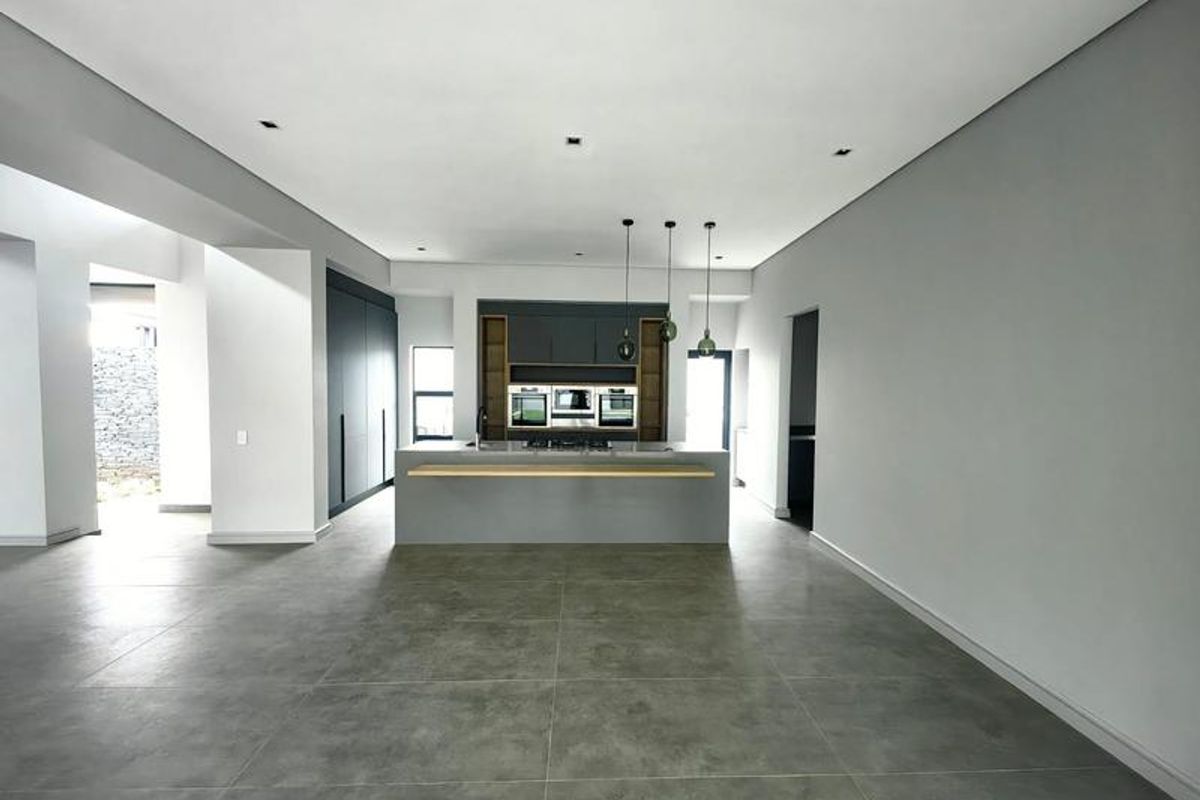 Modern, spacious kitchen featuring a central island, built-in ovens, sleek cabinetry, and large-format floor tiles in an open-plan layout.