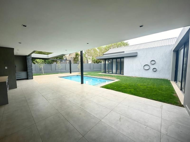 Spacious covered patio area featuring modern tiling, recessed lighting, and built-in cabinetry, overlooking a private swimming pool and landscaped garden.