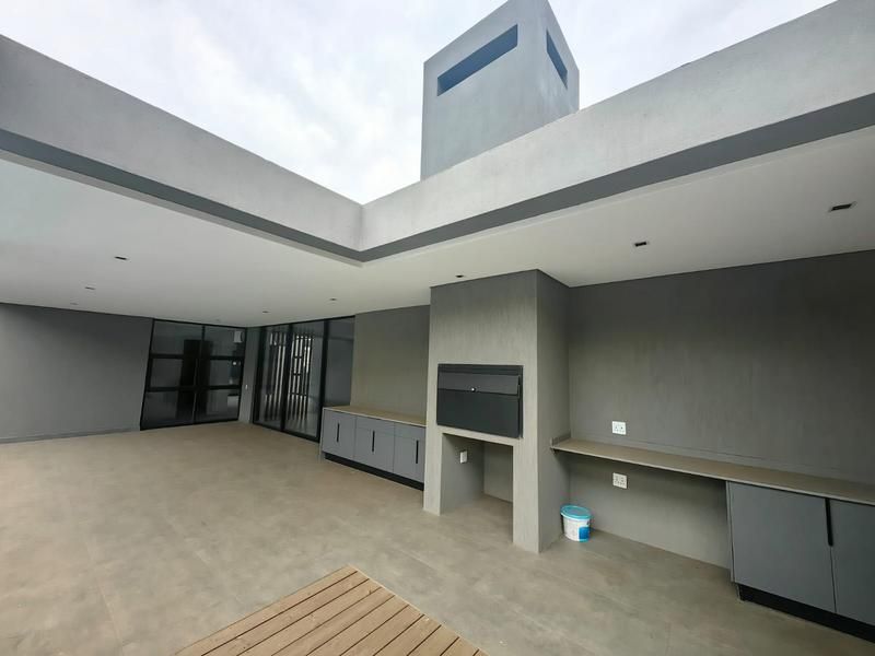 A modern covered patio featuring a built-in braai, sleek cabinetry, recessed lighting, and large sliding glass doors leading into the home.