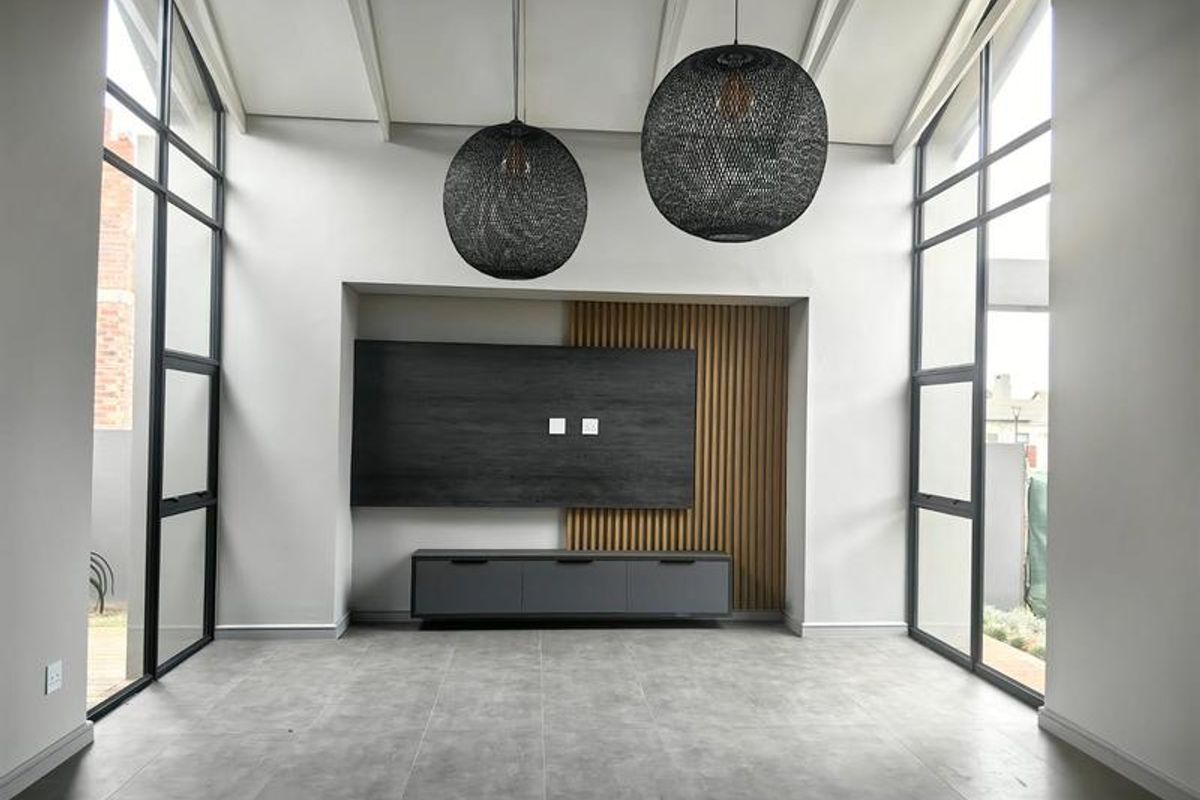 A bright, modern living room featuring a vaulted ceiling, large floor-to-ceiling windows, and a stylish built-in media wall with timber slat accents.