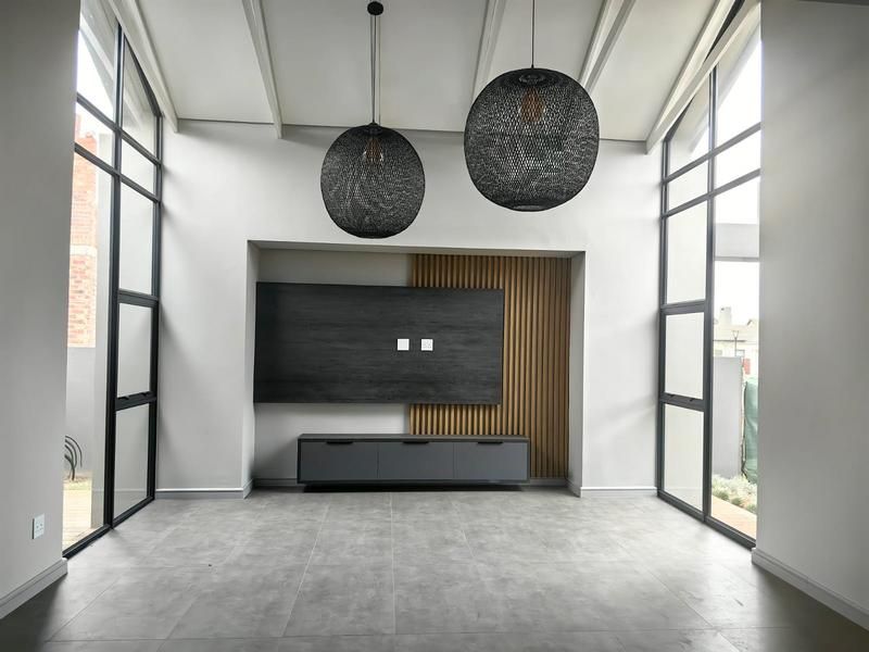 A bright, modern living room featuring a vaulted ceiling, large floor-to-ceiling windows, and a stylish built-in media wall with timber slat accents.