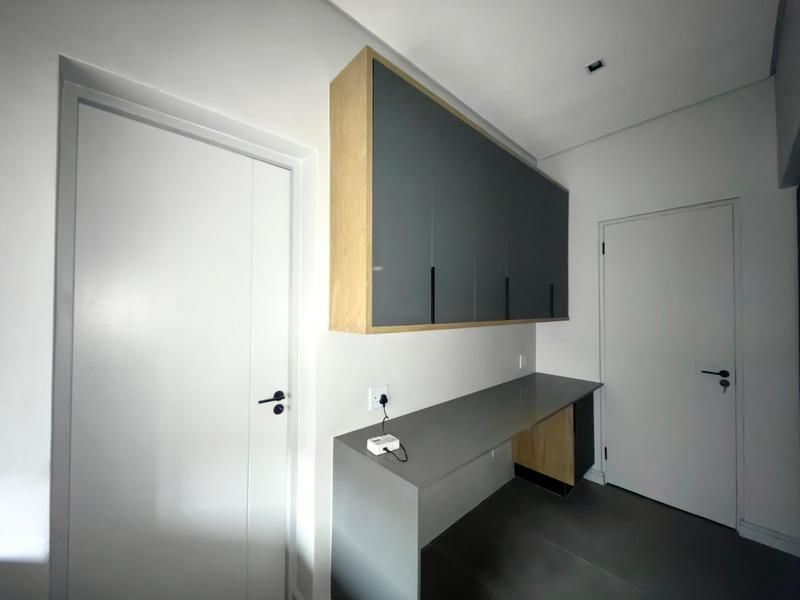 A modern, minimalist utility space or study nook featuring sleek grey built-in cabinetry, a matching desk surface, and clean, contemporary finishes.