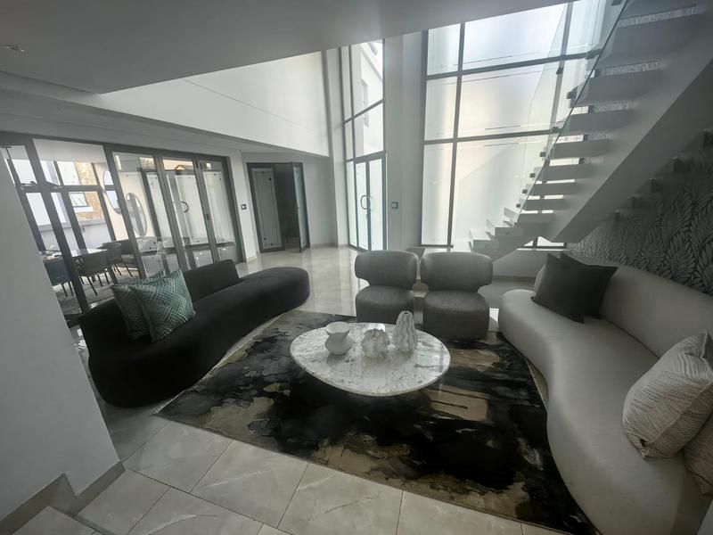 Spacious double-volume living area featuring a modern floating staircase with glass balustrade, large format floor tiles, and expansive floor-to-ceiling windows.