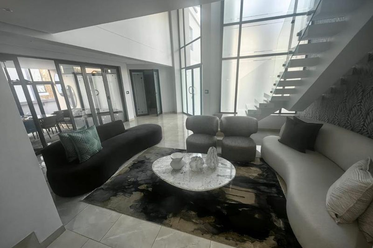 Spacious double-volume living area featuring a modern floating staircase with glass balustrade, large format floor tiles, and expansive floor-to-ceiling windows.