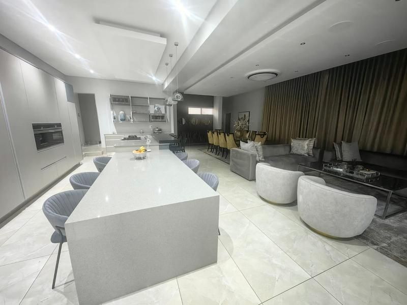 Spacious open-plan living area featuring a modern kitchen with a large stone island, integrated appliances, and seamless flow to the dining and lounge spaces.