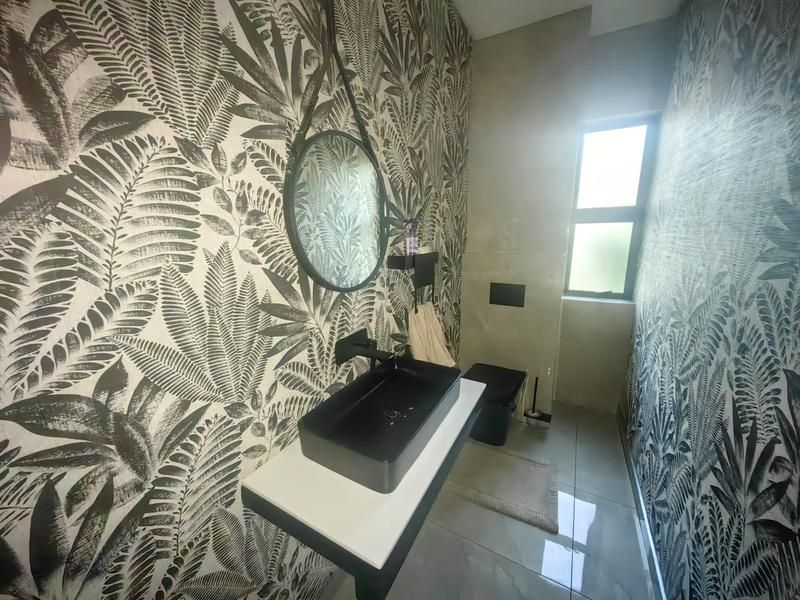 Modern bathroom featuring a wall-mounted vanity with a black vessel sink, wall-hung toilet, and striking botanical patterned wallpaper.