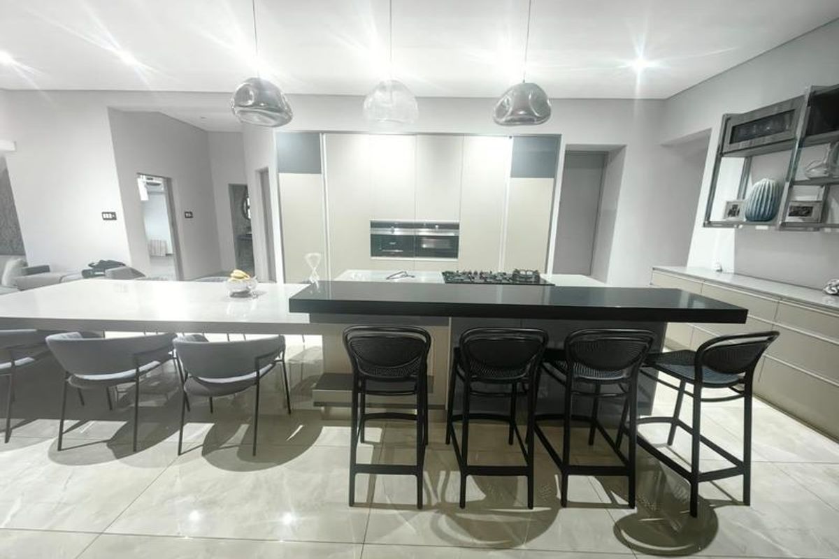 Modern open-plan kitchen featuring a large island with stone countertops, integrated gas hob, built-in ovens, and sleek cabinetry with contemporary pendant lighting.