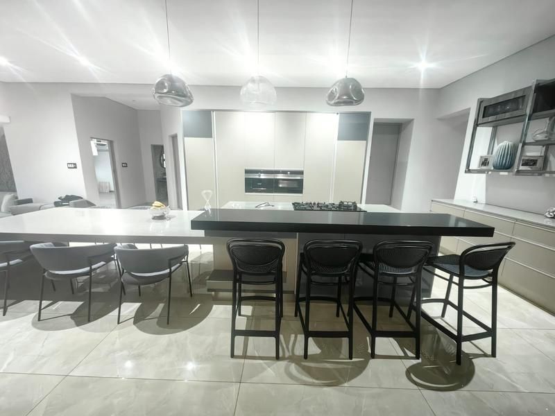 Modern open-plan kitchen featuring a large island with stone countertops, integrated gas hob, built-in ovens, and sleek cabinetry with contemporary pendant lighting.