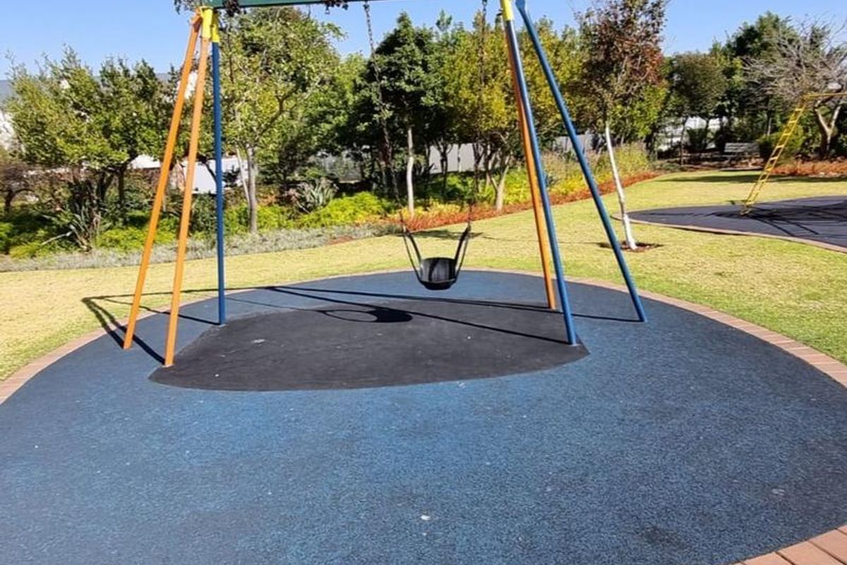 A well-maintained outdoor garden area featuring a dedicated playground section with rubberized safety flooring and a swing set.