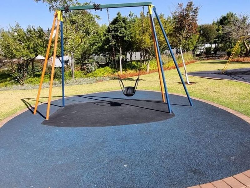 A well-maintained outdoor garden area featuring a dedicated playground section with rubberized safety flooring and a swing set.