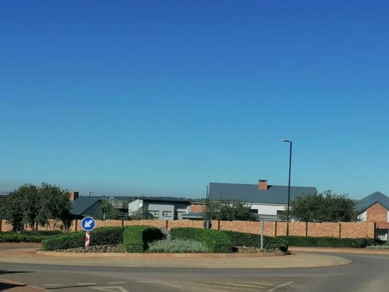 A view of the residential estate entrance featuring a landscaped roundabout and brick boundary wall.