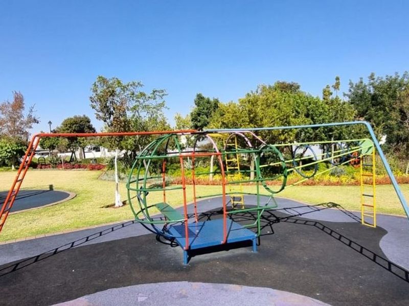 A well-maintained outdoor playground area featuring a metal climbing structure set on rubberized safety flooring within a landscaped garden setting.