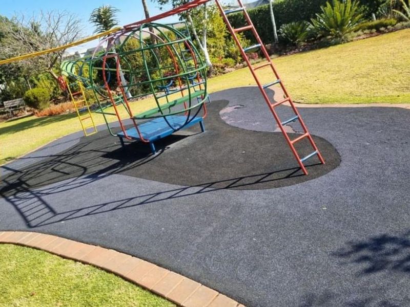 A well-maintained garden area featuring a dedicated playground section with rubberized safety surfacing and brick border edging.