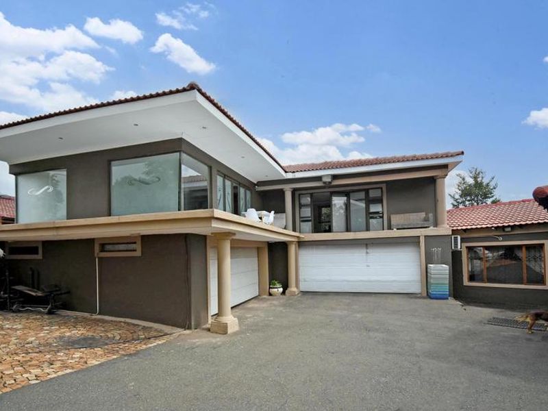 Front elevation of a modern double-story house featuring a paved driveway, double garage, and an upper-level balcony with sliding door access.