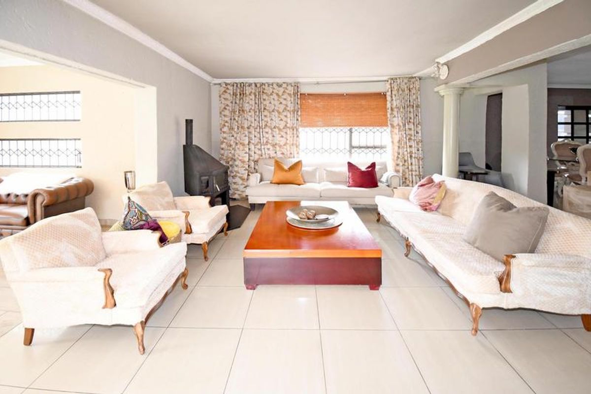 Spacious living room featuring large format floor tiles, a freestanding fireplace, and natural light through windows fitted with security bars.