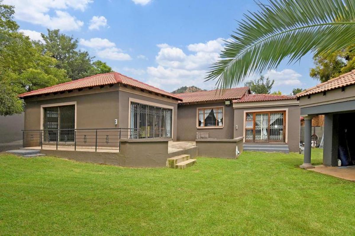 Rear view of the house featuring a raised patio, sliding glass doors with security gates, and a well-maintained lawn area.