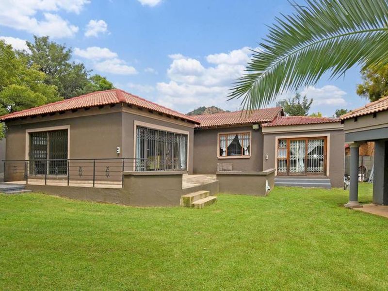Rear view of the house featuring a raised patio, sliding glass doors with security gates, and a well-maintained lawn area.