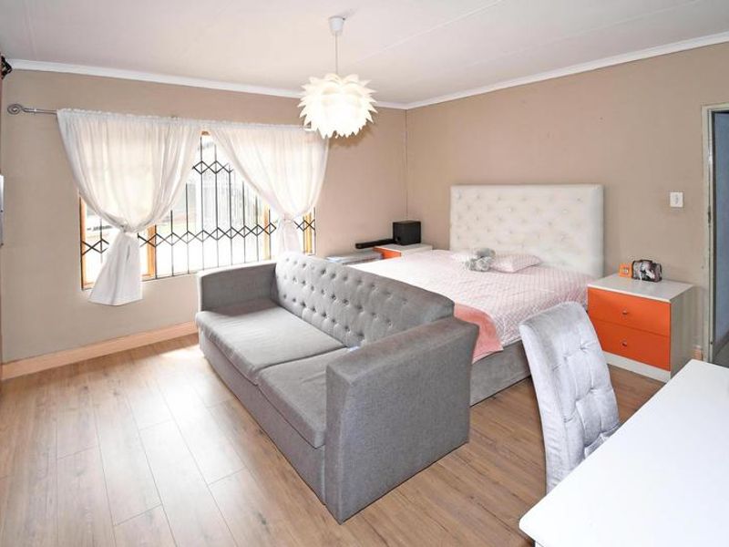 A bedroom featuring laminate flooring, a built-in wardrobe, and a window fitted with a security gate.