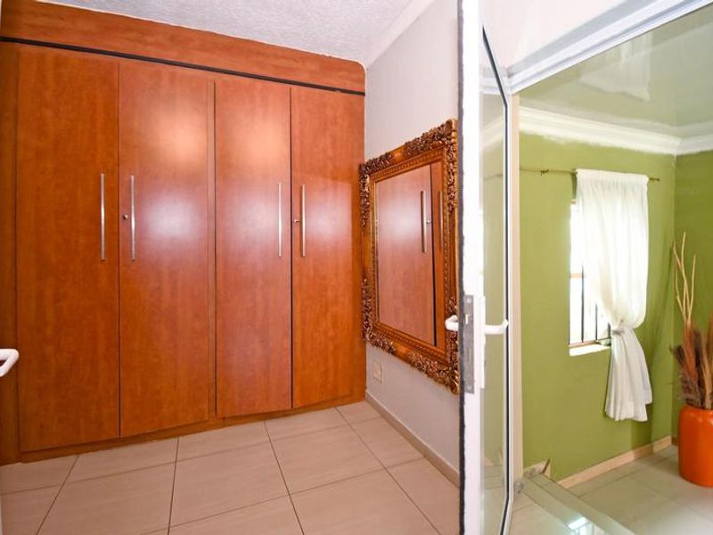Bedroom featuring built-in wooden cupboards and tiled flooring, with an adjacent view into a secondary room with green walls.