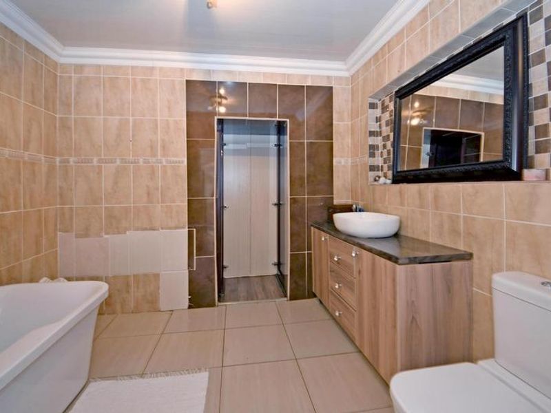 A bathroom featuring a freestanding bathtub, vanity with vessel sink, and toilet, currently requiring repairs to the wall tiling.