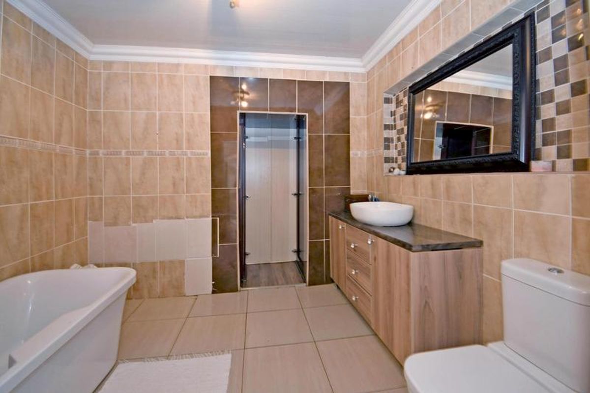 A bathroom featuring a freestanding bathtub, vanity with vessel sink, and toilet, currently requiring repairs to the wall tiling.