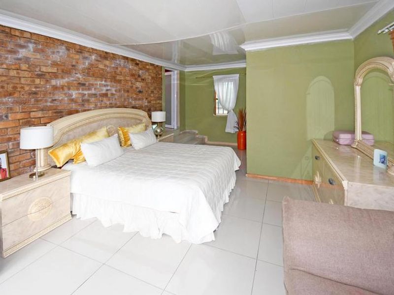Spacious bedroom featuring an exposed brick accent wall, glossy tiled flooring, and a high-gloss ceiling finish with crown molding.