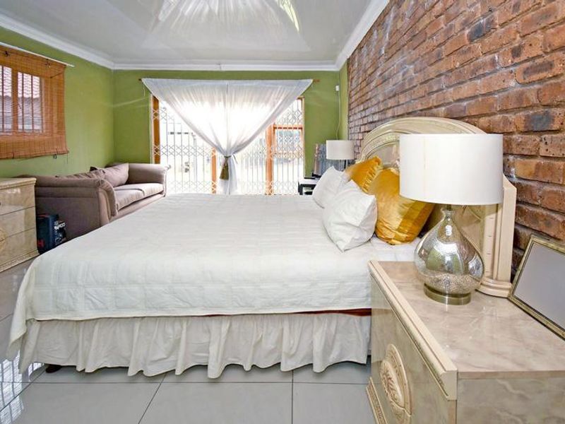 Spacious bedroom featuring an exposed brick accent wall, neutral tiled flooring, and direct access to the exterior through a secure sliding door.
