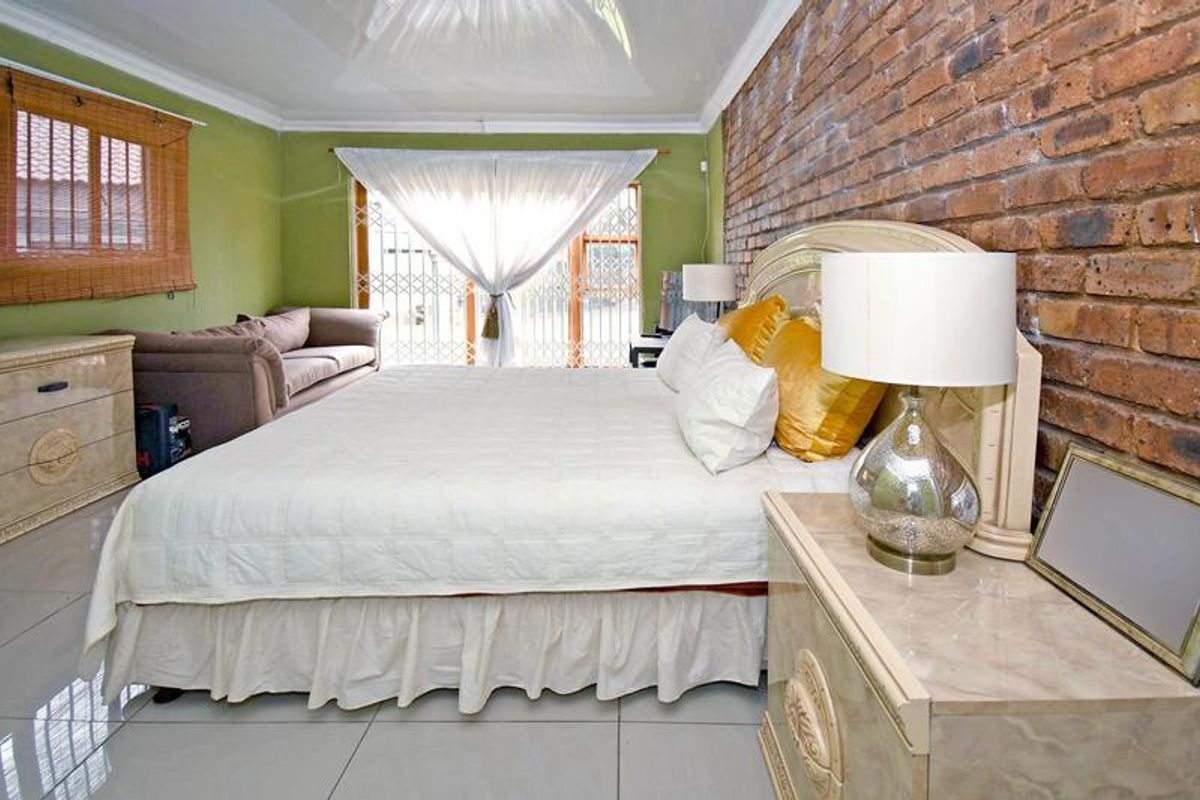 Spacious bedroom featuring an exposed brick accent wall, neutral tiled flooring, and direct access to the exterior through a secure sliding door.