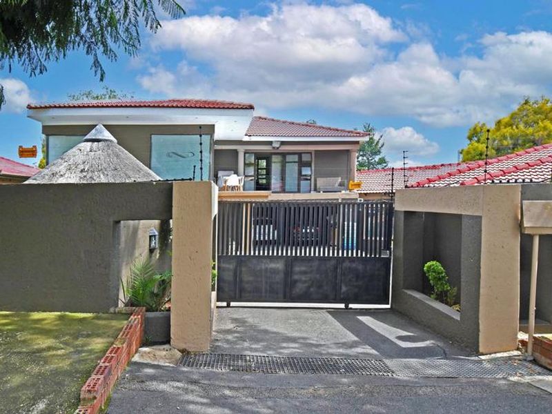 Front exterior view of the property featuring a secure sliding gate, concrete driveway, and perimeter wall with integrated electric fencing.