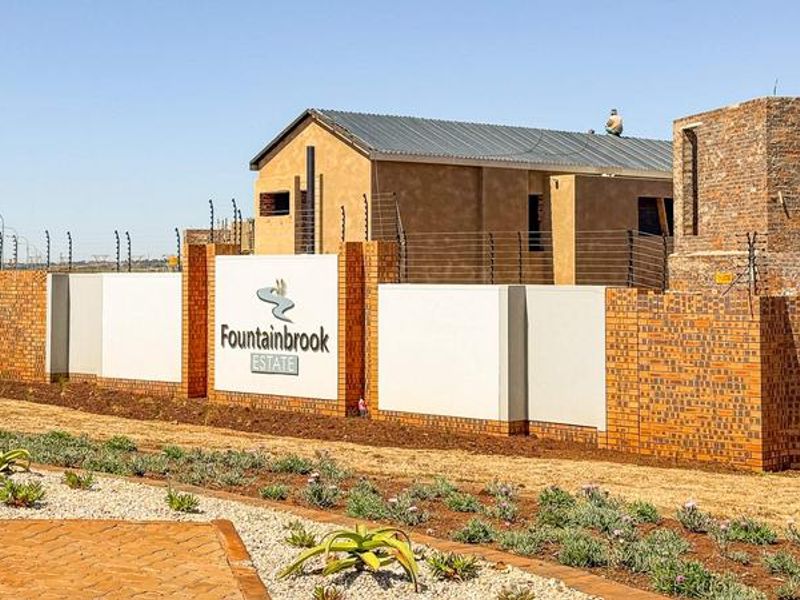 Entrance view of Fountainbrook Estate featuring brick boundary walls, electric fencing, and ongoing construction of residential units.