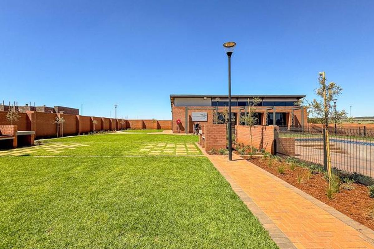 A well-maintained communal clubhouse area featuring a brick building, swimming pool, paved walkways, and built-in braai facilities within a secure estate setting.