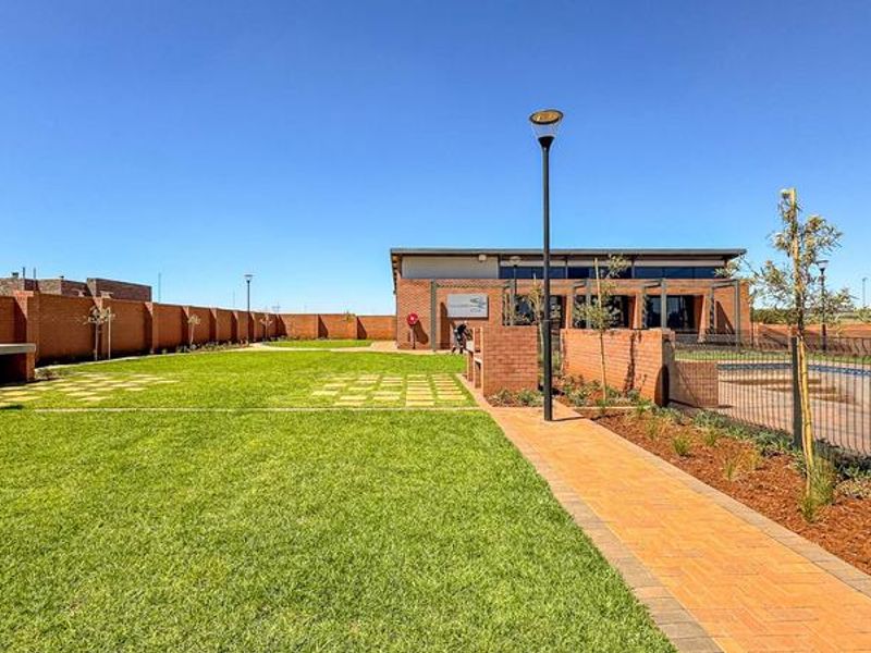 A well-maintained communal clubhouse area featuring a brick building, swimming pool, paved walkways, and built-in braai facilities within a secure estate setting.