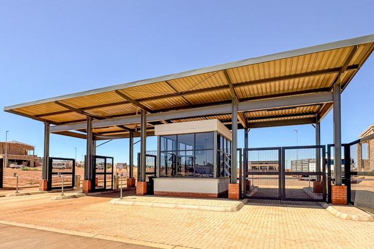 A modern security entrance gatehouse featuring a metal roof structure, steel support columns, and automated security gates at the estate entrance.