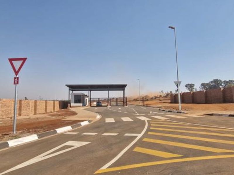 View of the entrance gatehouse and perimeter wall of a residential estate with paved roads and street infrastructure.