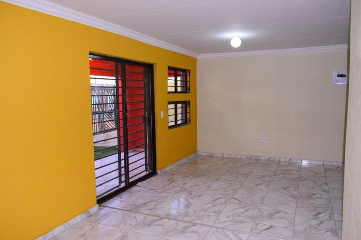 An empty living room featuring tiled flooring, bright yellow accent walls, and a sliding glass door with integrated security gate leading to the exterior.