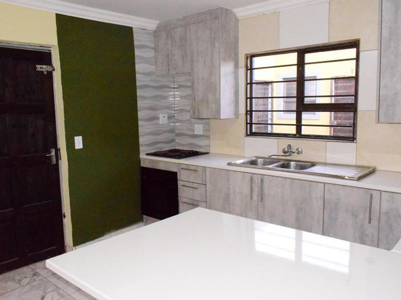 A functional kitchen featuring light-toned cabinetry, a built-in hob and oven, double sink, and security bars on the window.