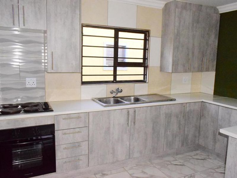 A clean, modern kitchen featuring light grey wood-look cabinetry, built-in oven and hob, double sink, and tiled splashback with neutral wall finishes.
