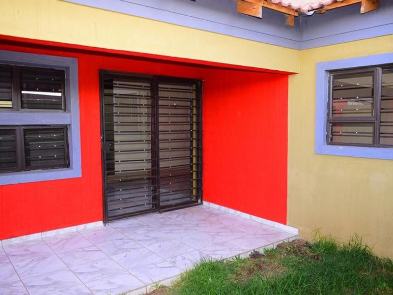 A covered patio area featuring tiled flooring, sliding glass doors with security gates, and aluminium window frames with security bars.
