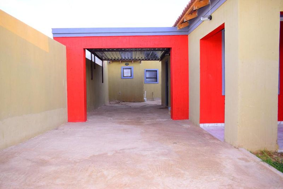 A rear exterior view of the property featuring a concrete driveway, a covered carport area, and boundary walls with a tiled roof section.