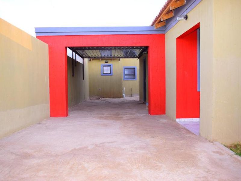 A rear exterior view of the property featuring a concrete driveway, a covered carport area, and boundary walls with a tiled roof section.