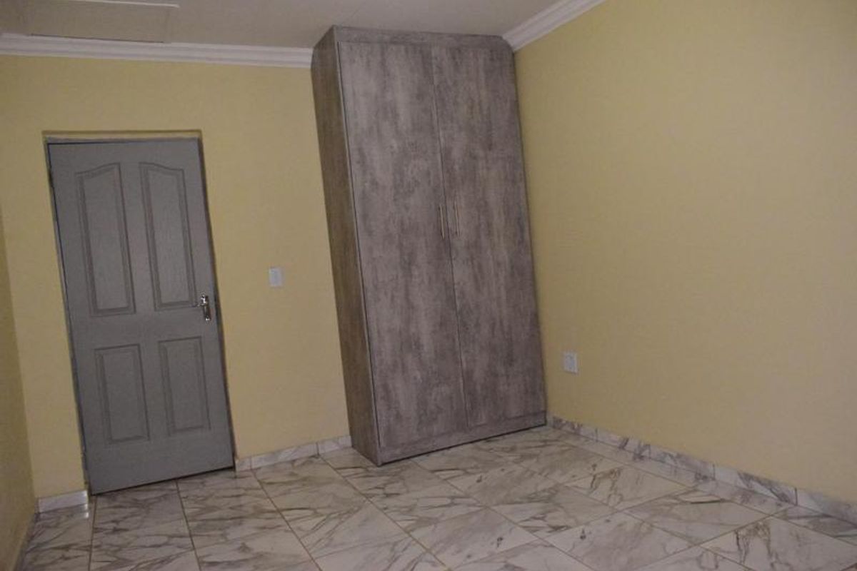 A clean, empty bedroom featuring modern marble-look tiled flooring, a built-in wardrobe with a textured finish, and neutral wall paint.