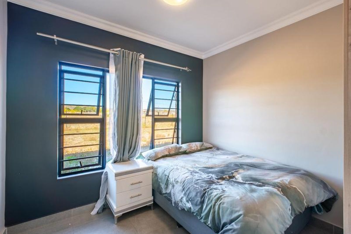 A well-lit bedroom featuring tiled flooring, cornicing, and large top-hung windows with security bars, offering a clear view of the surrounding landscape.