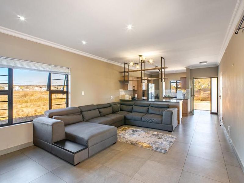 Spacious open-plan living area featuring tiled floors, recessed lighting, and a modern kitchen with a central island, seamlessly connecting to the outdoor space.