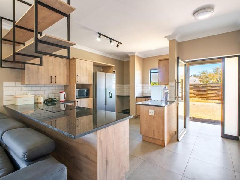 Modern open-plan kitchen featuring wood-finish cabinetry, granite countertops, subway tile backsplash, and direct access to the outdoor area.