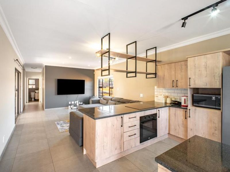 Modern open-plan living area featuring a contemporary kitchen with light wood cabinetry, stone countertops, and integrated appliances, flowing into a comfortable lounge space.