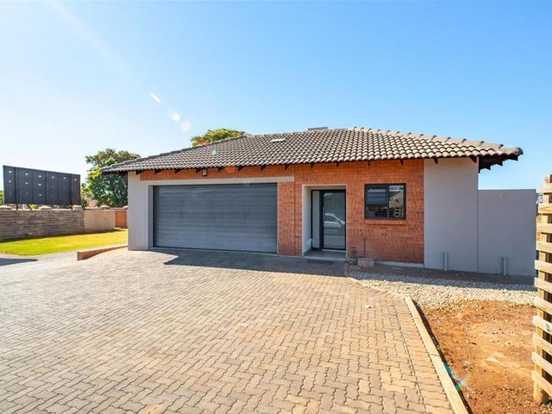 Front exterior view of a modern townhouse featuring a brick facade, tiled roof, automated garage, and a paved driveway.
