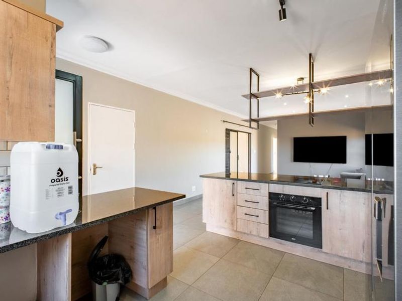 Modern kitchen featuring light wood-tone cabinetry, dark granite countertops, built-in oven, and a stylish suspended shelving unit over the breakfast bar area.