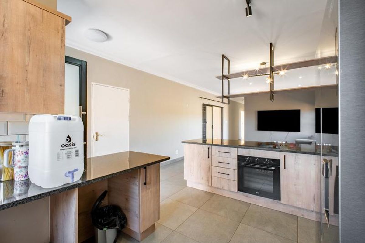 Modern kitchen featuring light wood-tone cabinetry, dark granite countertops, built-in oven, and a stylish suspended shelving unit over the breakfast bar area.