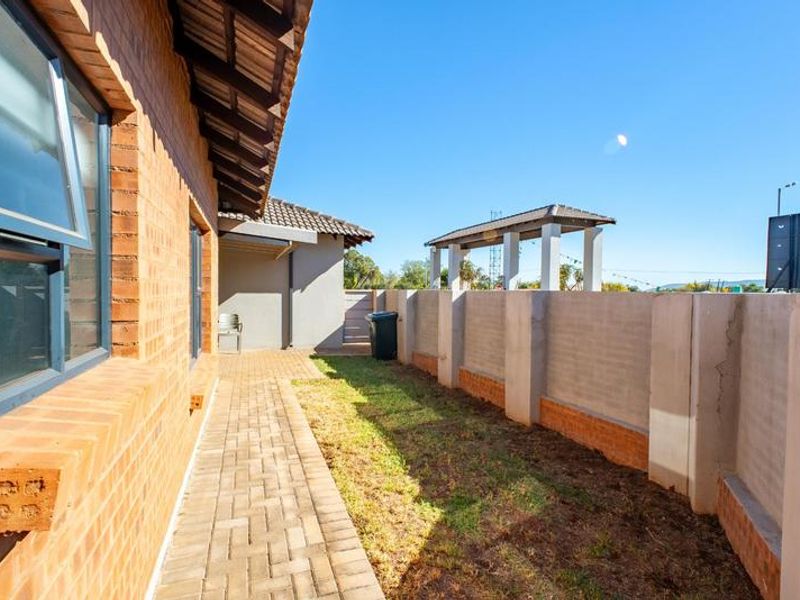 Rear exterior view of the townhouse featuring a brick paved walkway, small garden area, and a perimeter boundary wall.