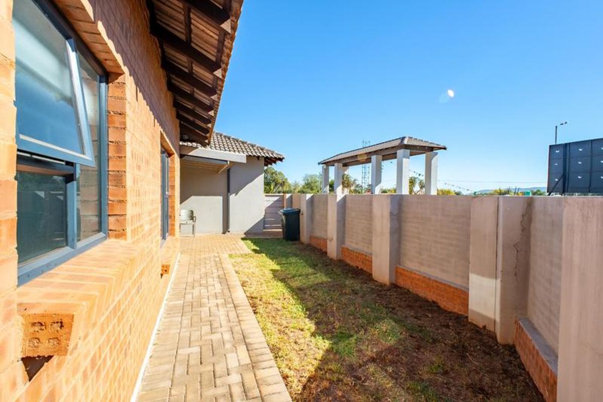 Rear exterior view of the townhouse featuring a brick paved walkway, small garden area, and a perimeter boundary wall.